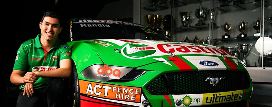 Professioneller Motorsportfahrer mit DBA-gesponsertem Supercars-Championship-Fahrzeug, das Rennpartnerschaft und Hochleistungsbremstechnologie zeigt Lächelnder Rennfahrer im grünen Teamshirt neben einem von DBA gesponserten grünen Ford Mustang Rennwagen mit mehreren Sponsorenlogos im Pokalraum